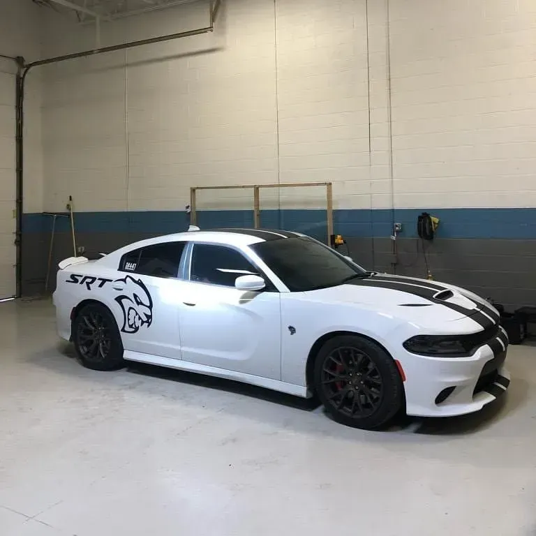 White Dodge Charger SRT with black racing stripes and wolf decal, parked indoors in a warehouse.
