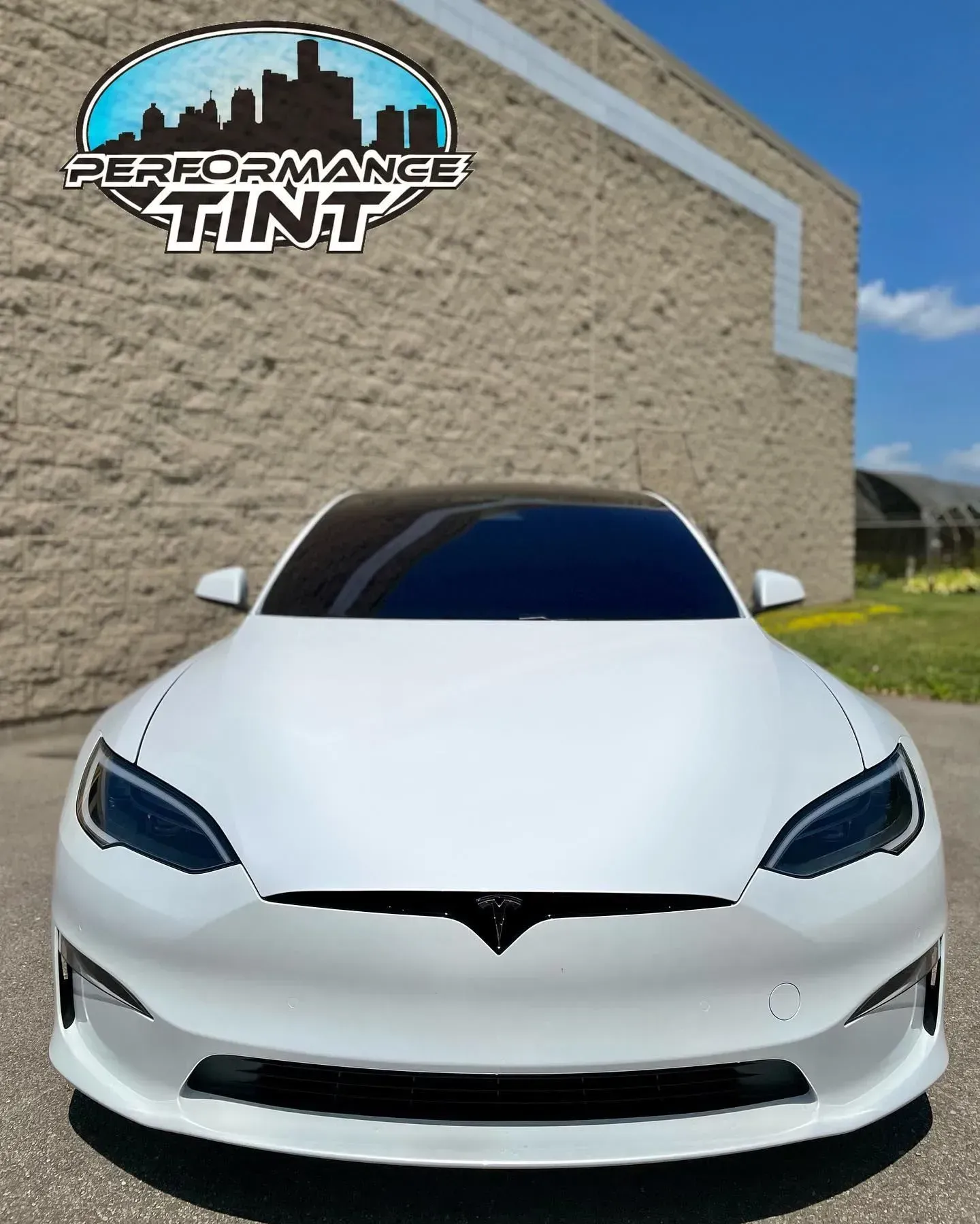 White Tesla parked in front of a beige wall with a Performance Tint logo overlay