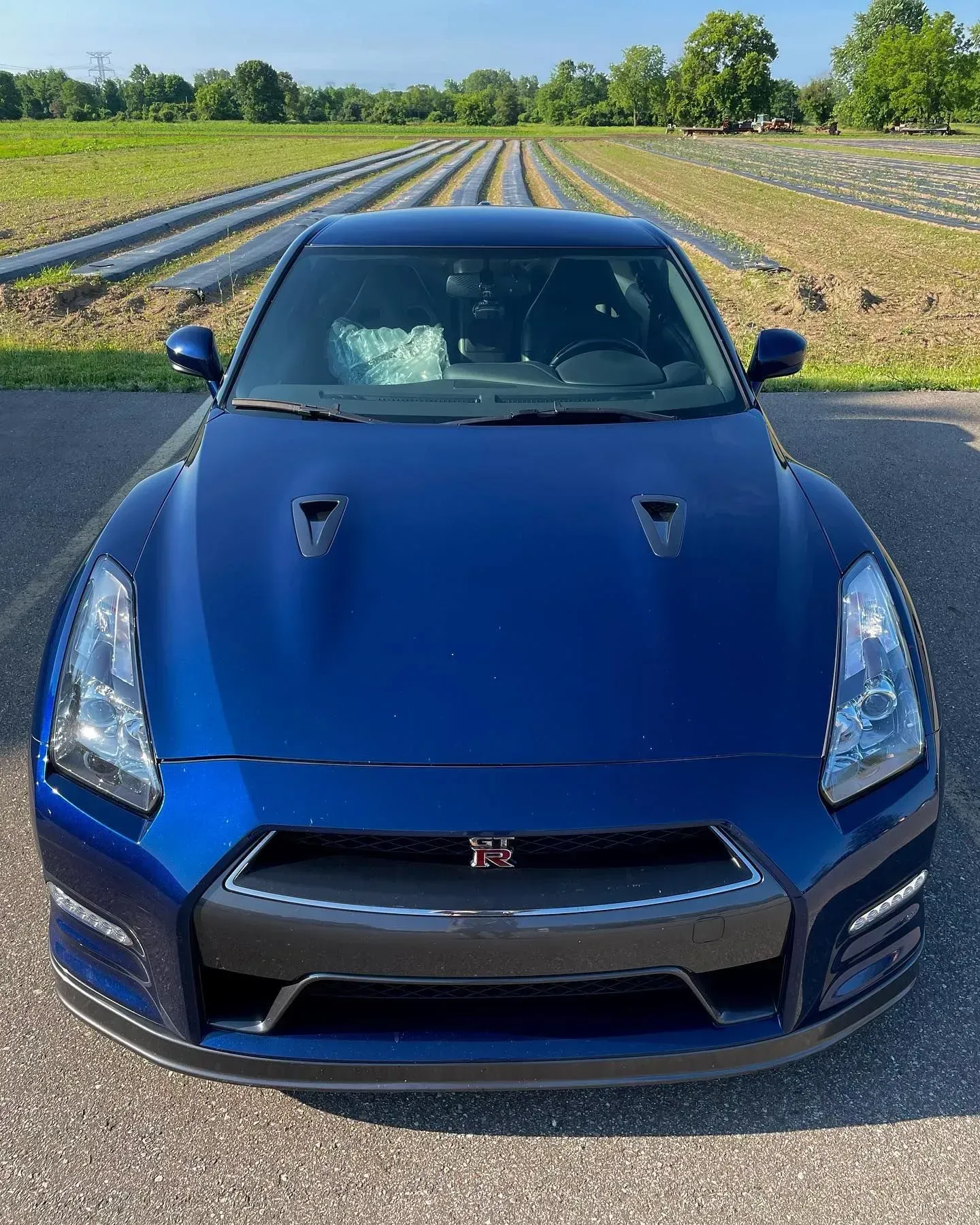 Blue Nissan GT-R parked on a rural road with fields and trees in the background