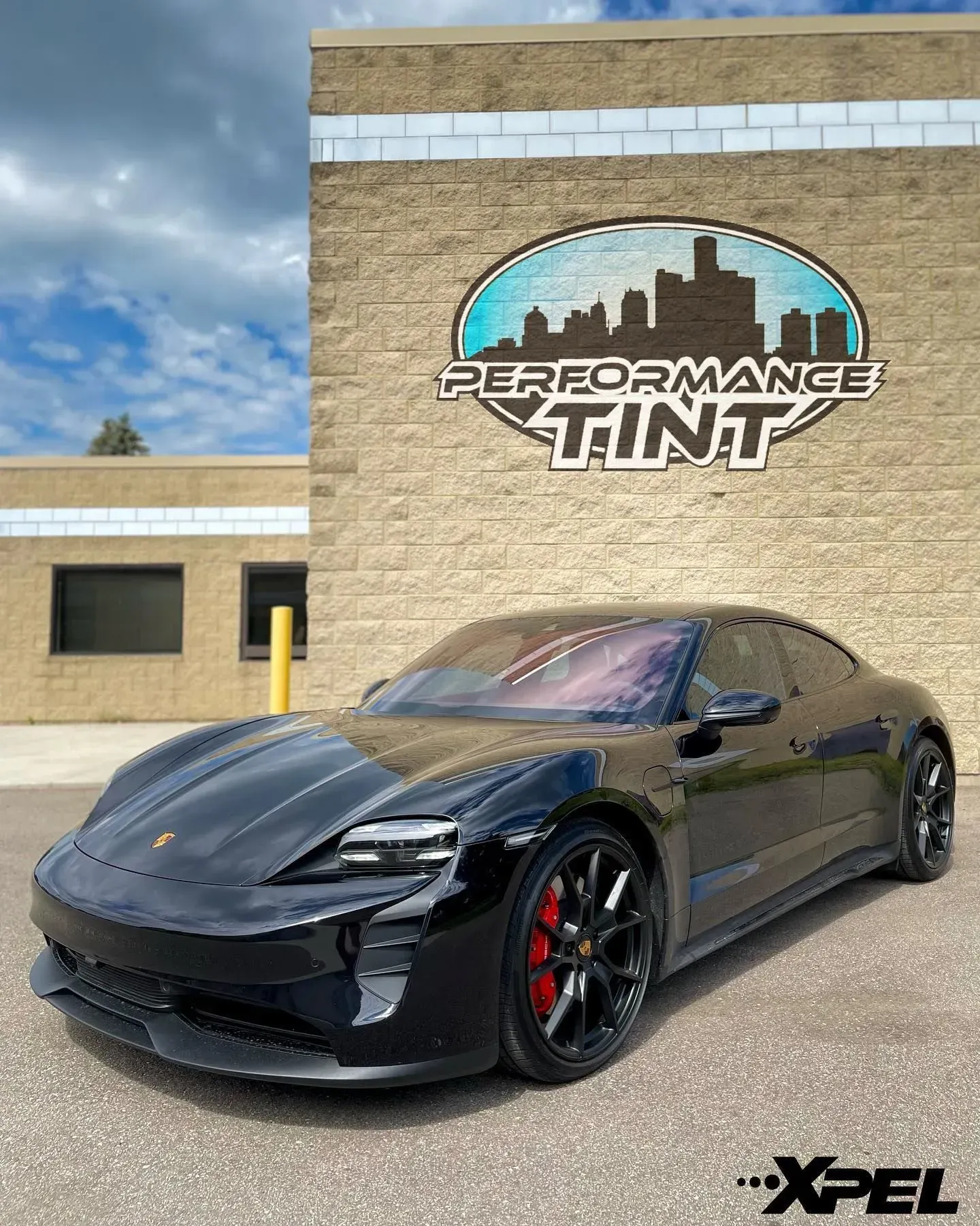 Black sports car parked in front of Performance Tint shop, with XPEL logo visible