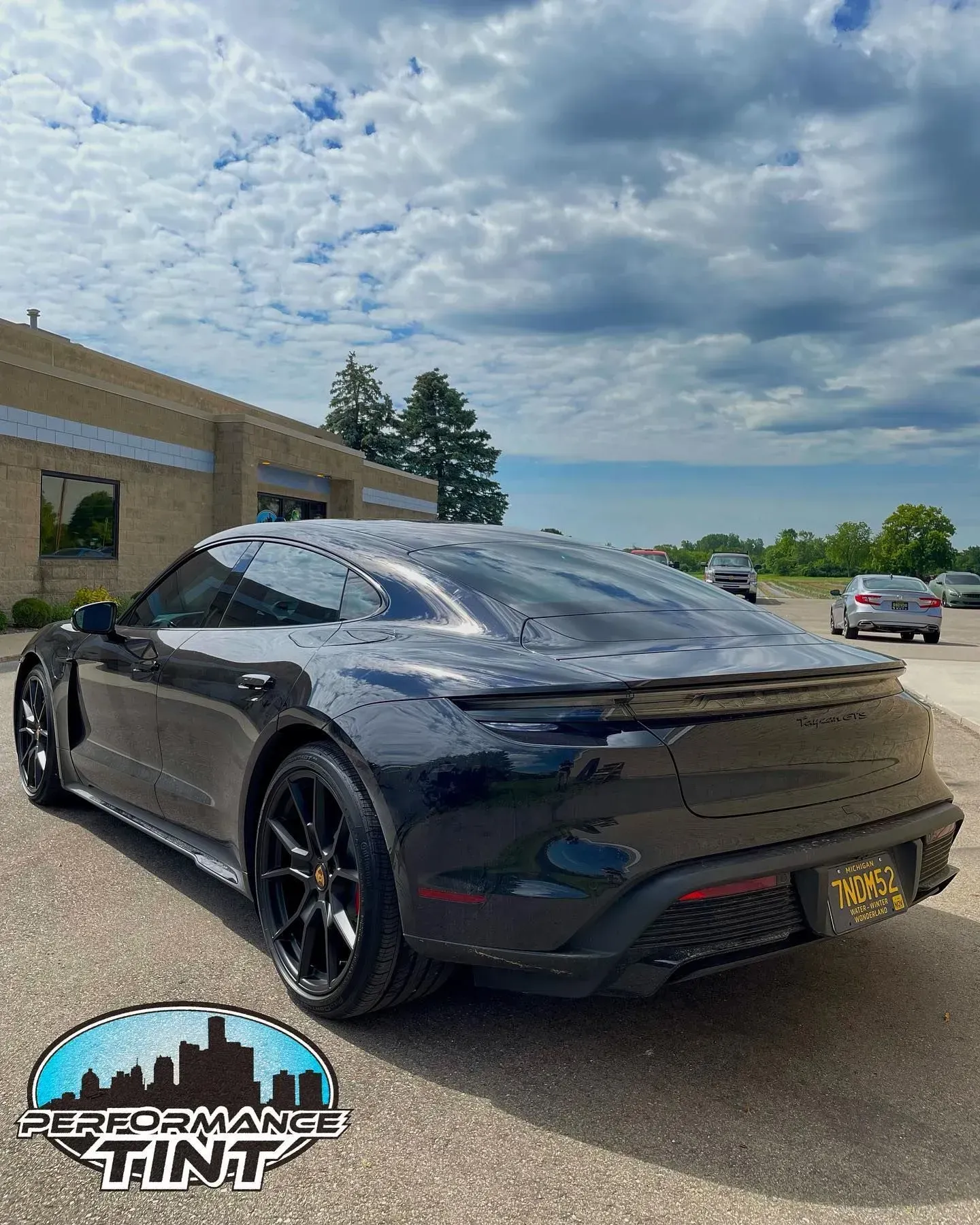 Black sports coupe parked outside a building under a cloudy sky, rear three-quarter view