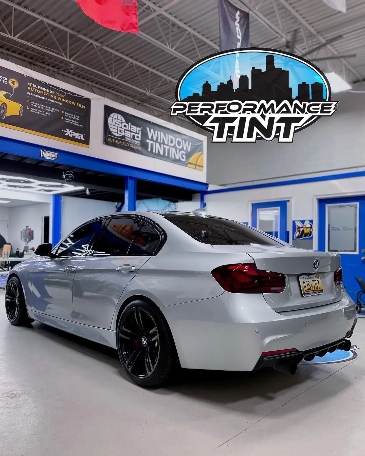 Silver sedan in a tint shop with black wheels, under a Performance Tint sign.
