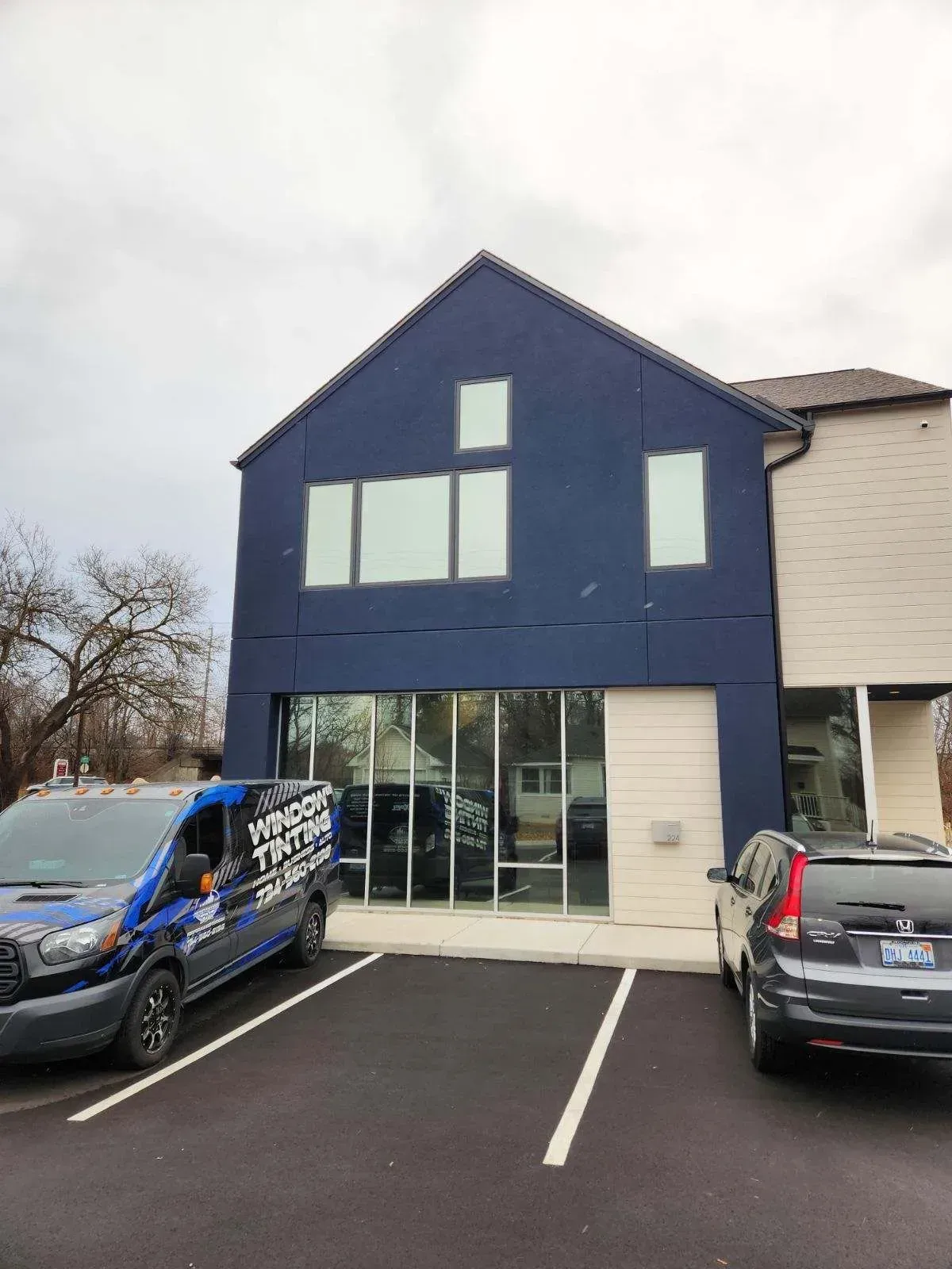 Blue commercial building with large windows and parked vans in front