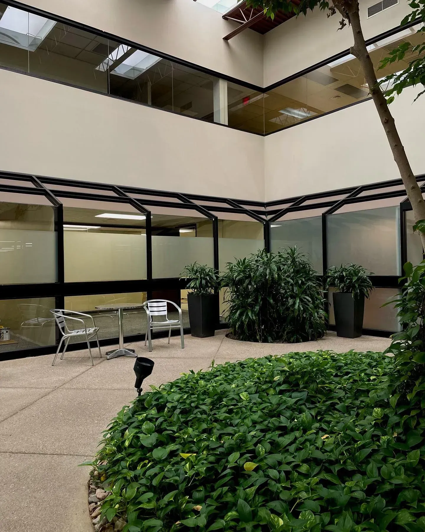 Courtyard patio with chairs, tables, planter, and beige building balconies surrounding a leafy courtyard.