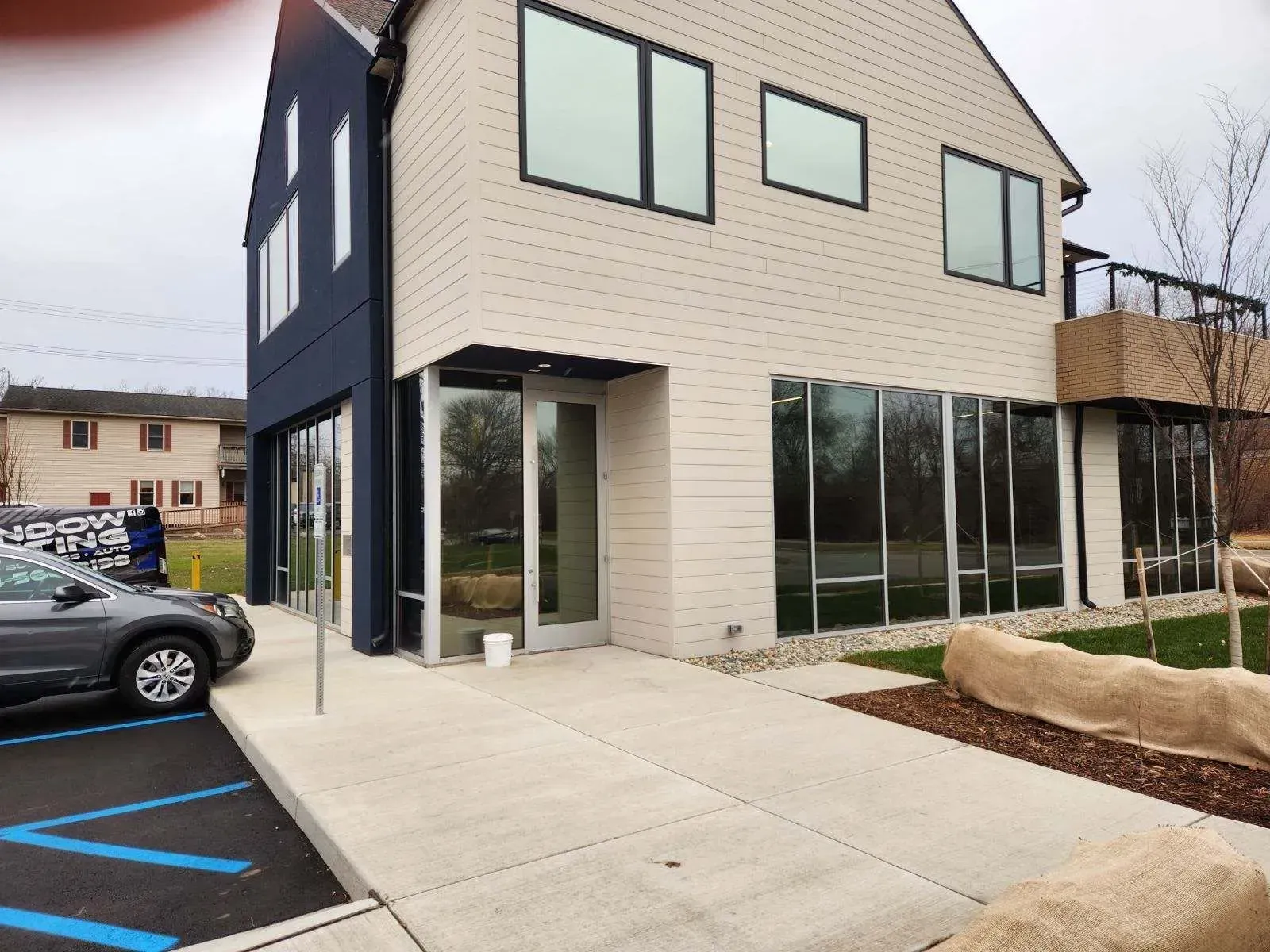Modern two-story building with beige siding, large windows, and parking spaces outside