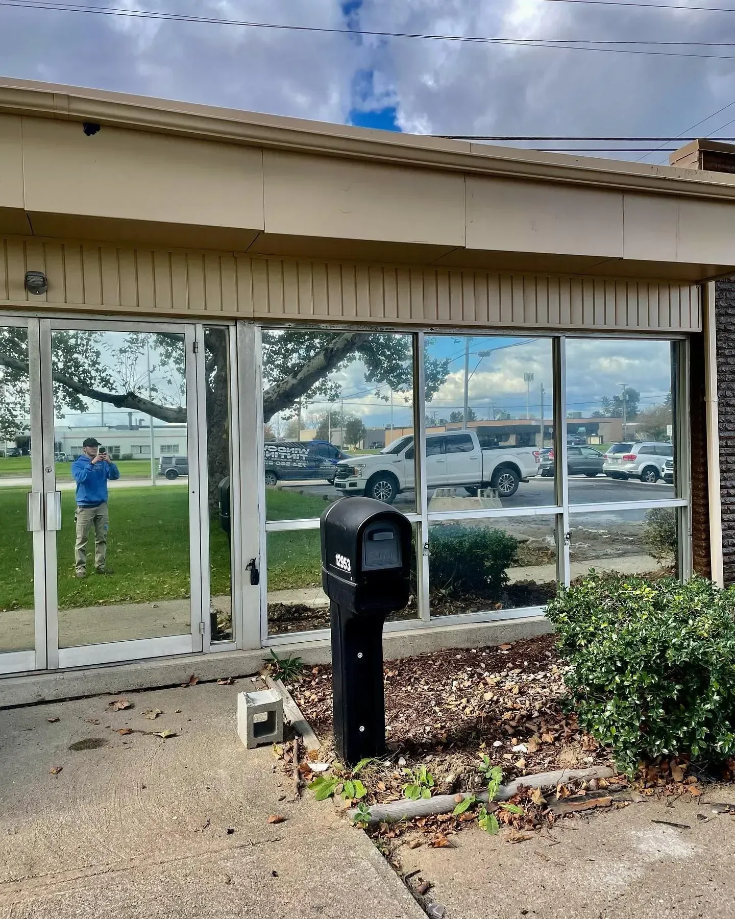 Outdoor mailbox by a building entrance, with parked vehicles and a cloudy sky in the background.