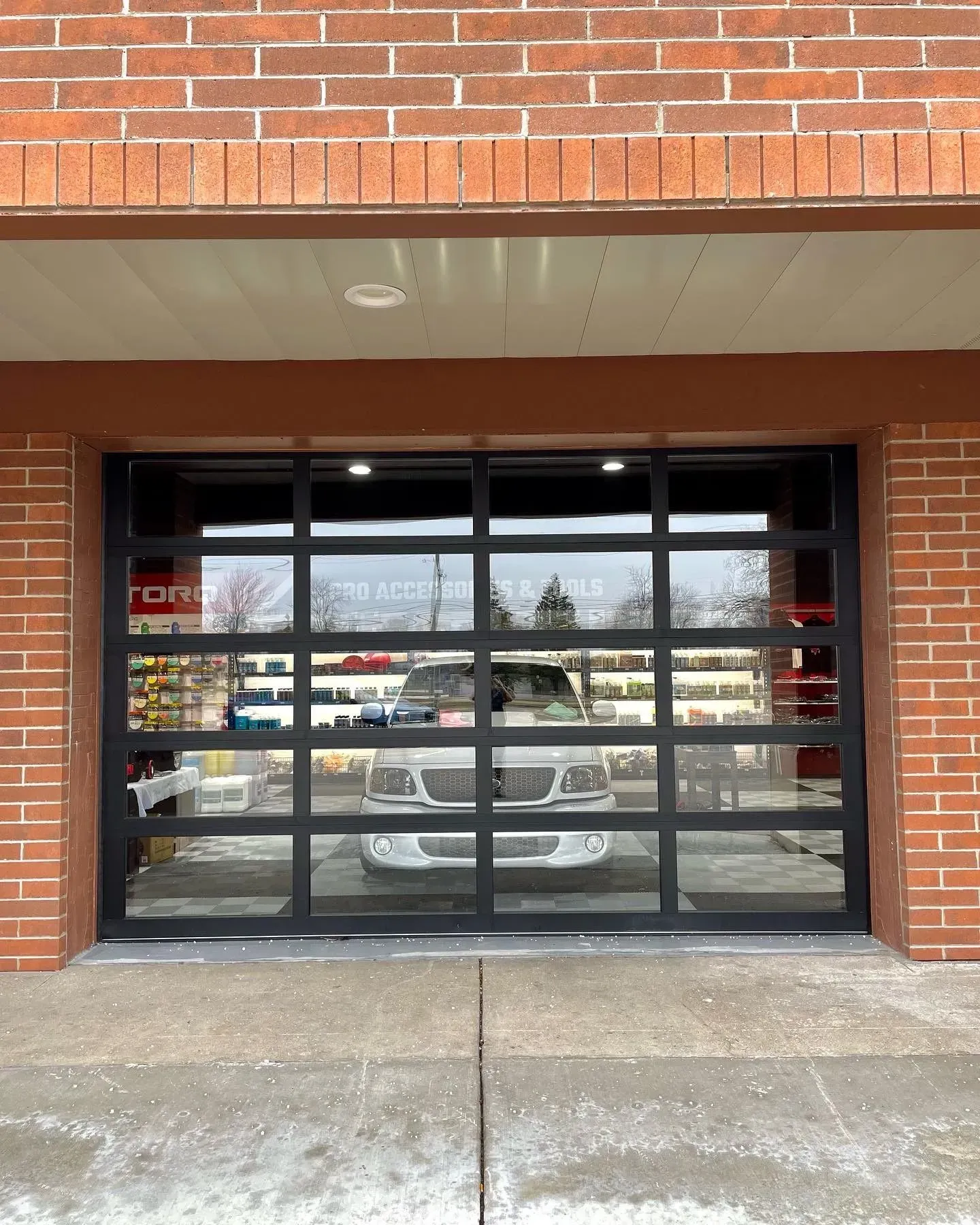 Glass storefront with black-framed windows reflecting parked cars in a brick building.