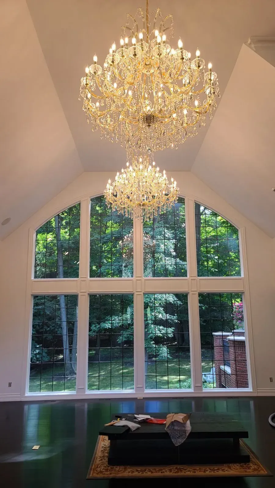 Elegant chandelier-lit room with tall arched windows, white walls, and a dark table below.