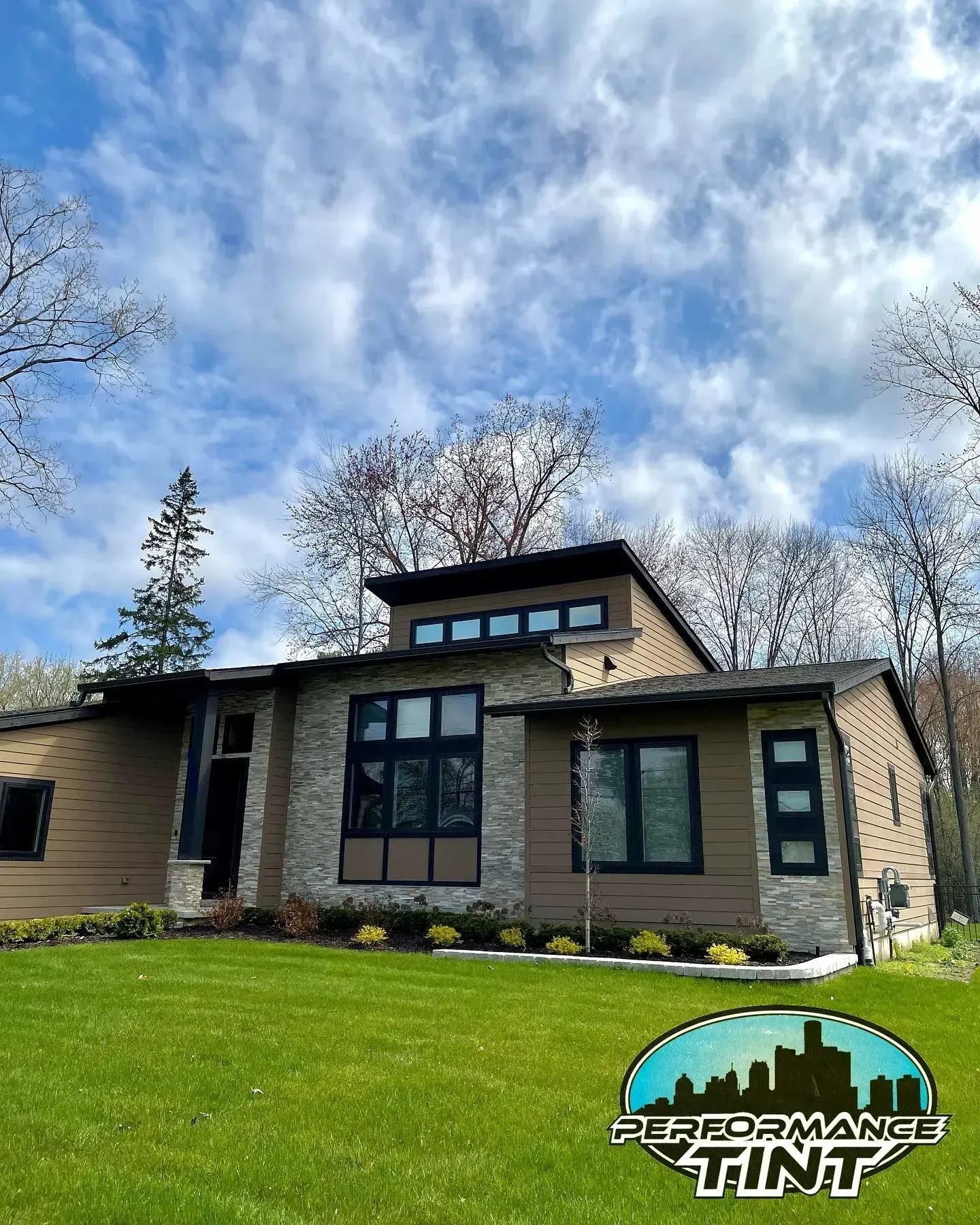 Modern tan house with black trim, large windows, green lawn, and cloudy sky; Performance Tint logo bottom right