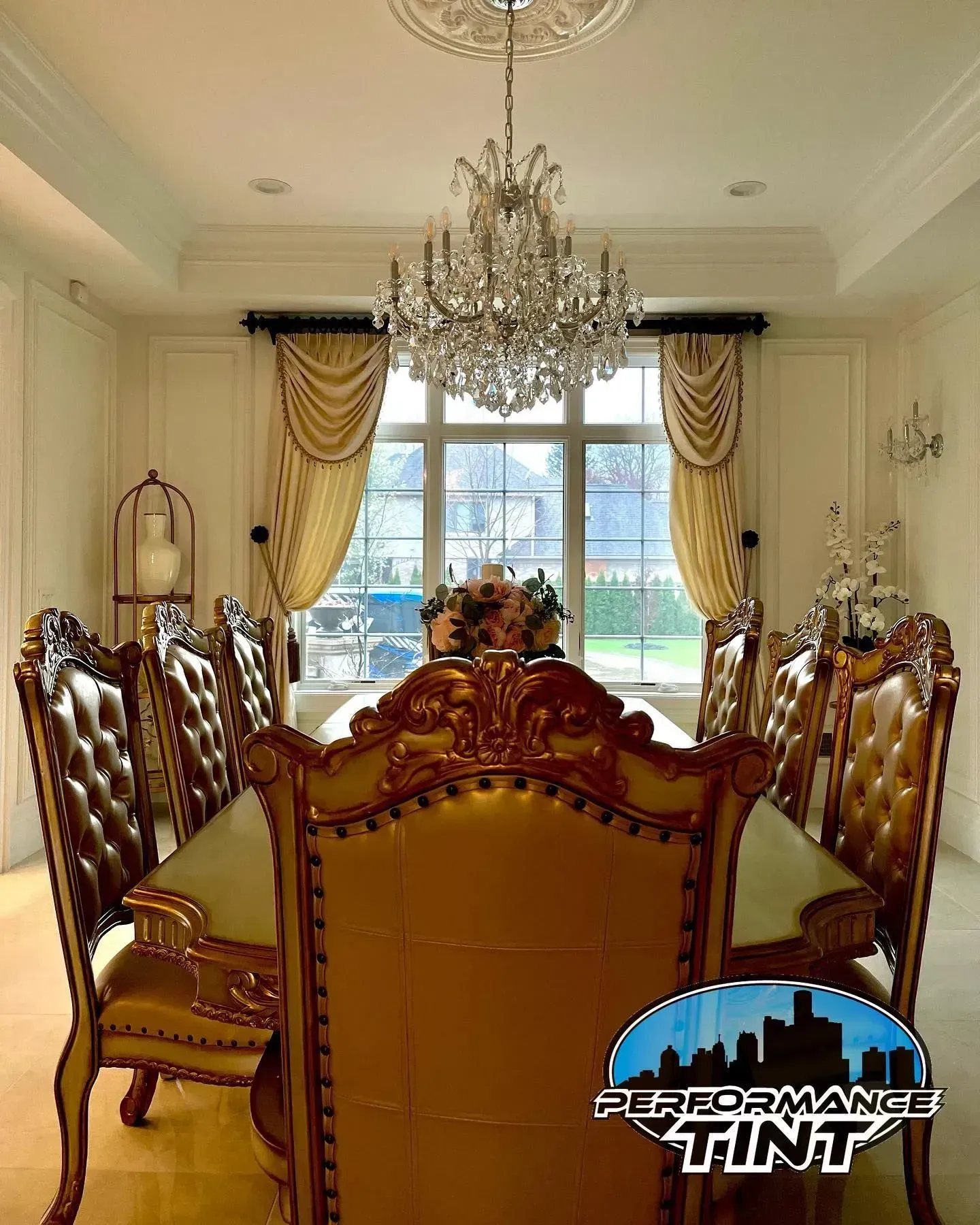 Elegant dining room with chandelier, ornate chairs, gold curtains, and large window view