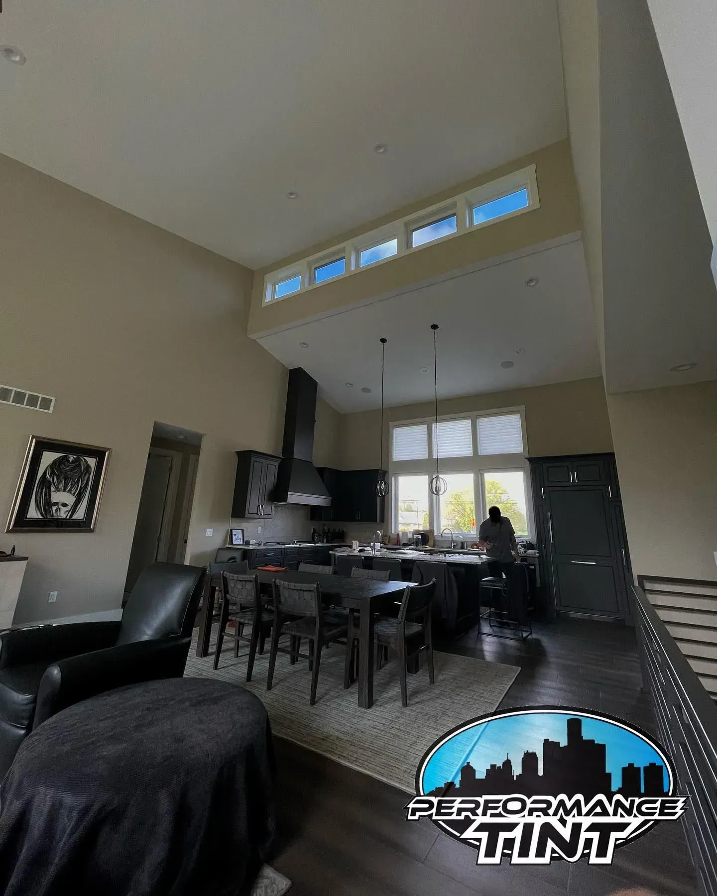 Spacious modern living room with high ceiling, dark furniture, and kitchen area in the background
