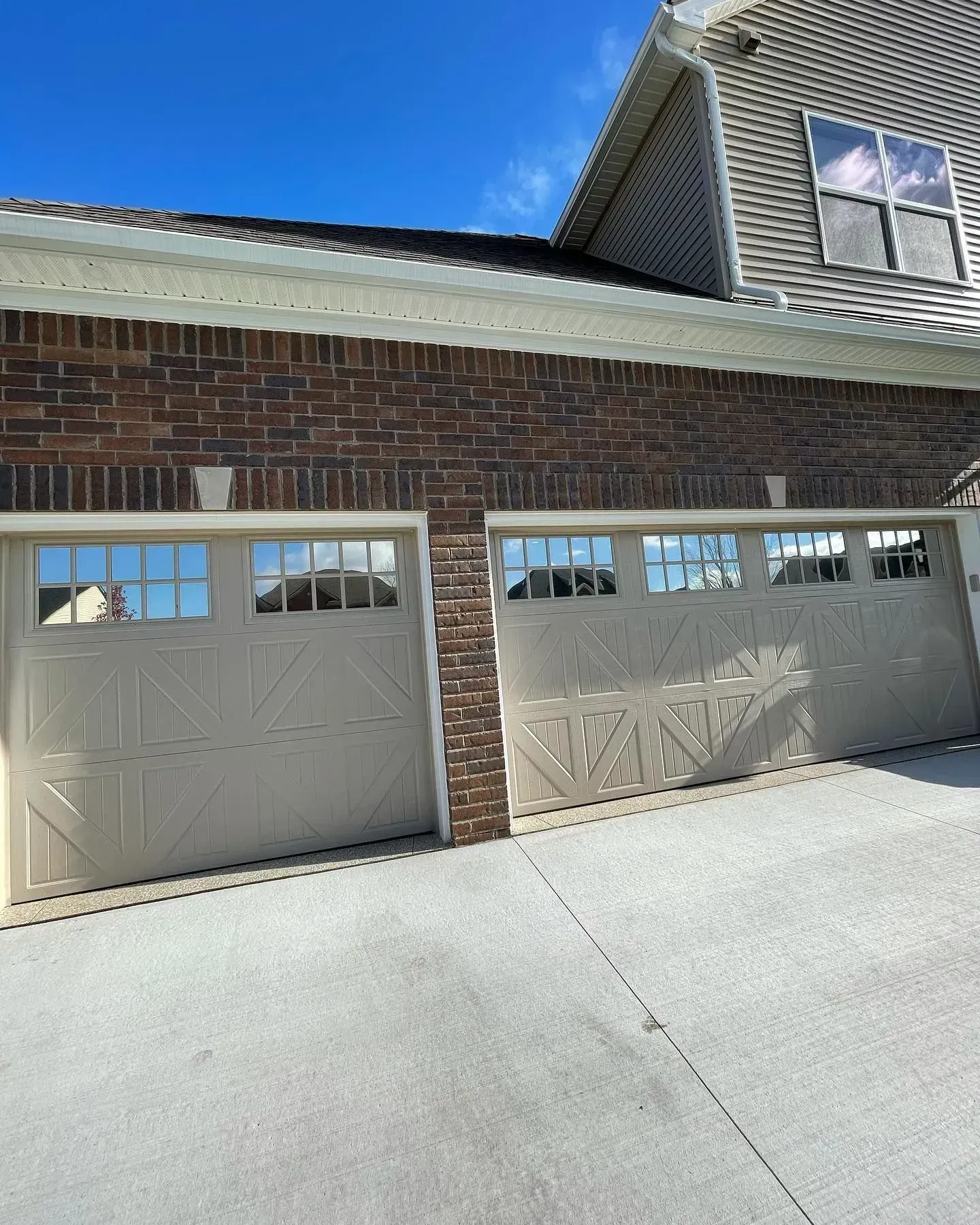 Two beige garage doors on a brick house under a bright blue sky