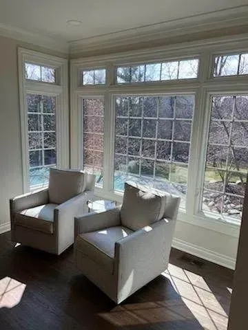 Bright sunroom with two white armchairs by large windows and a dark wood floor