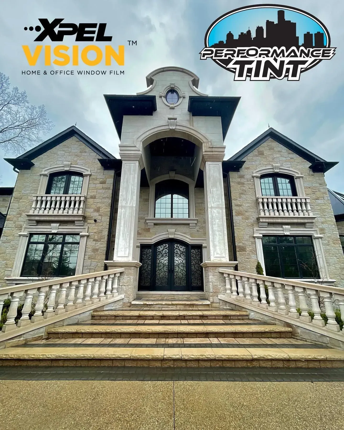 Stone house facade with large windows, central entrance, and XPEL Vision and Professional Tint logos above