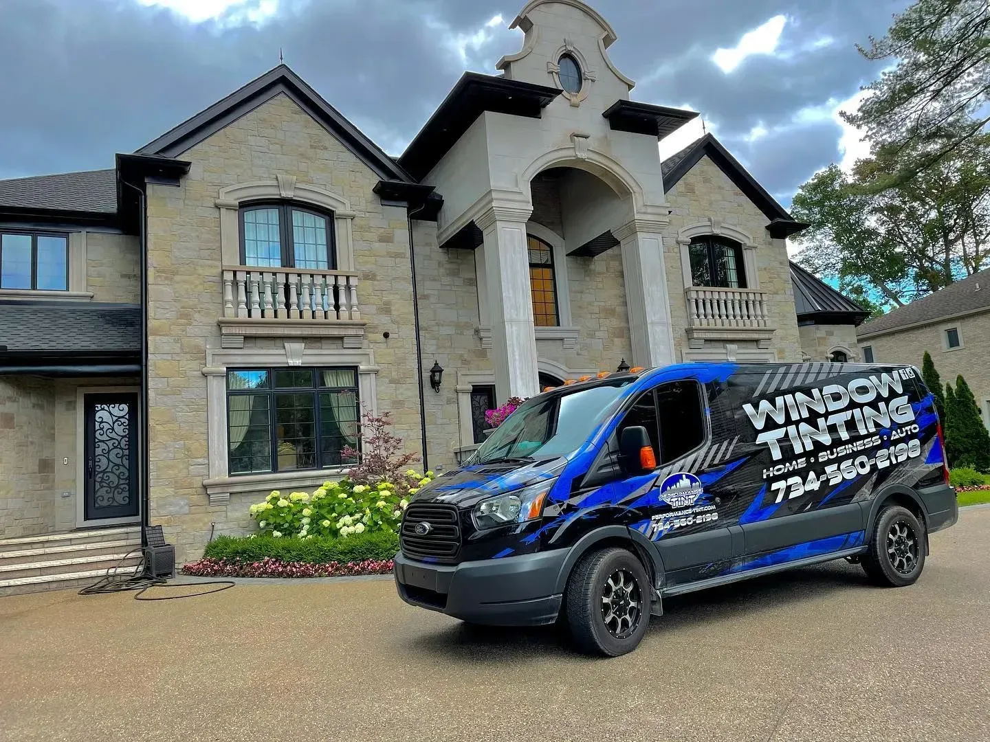 Blue window tinting van parked in front of a large stone house with an arched entryway