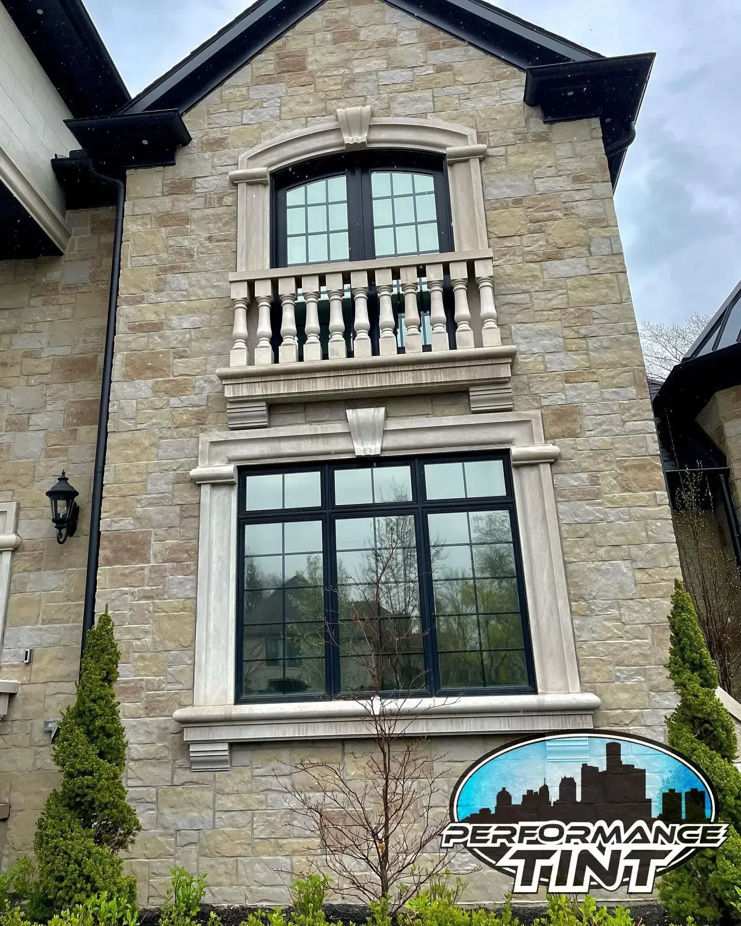 Stone house facade with large window and balcony, dark-framed windows, and a “Performance Tint” logo at bottom right