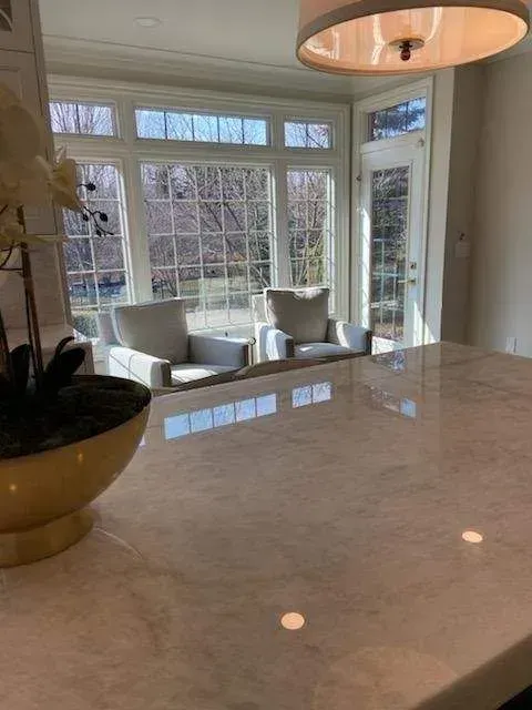 Bright dining area with a marble countertop, pendant lights, and large windows overlooking trees.