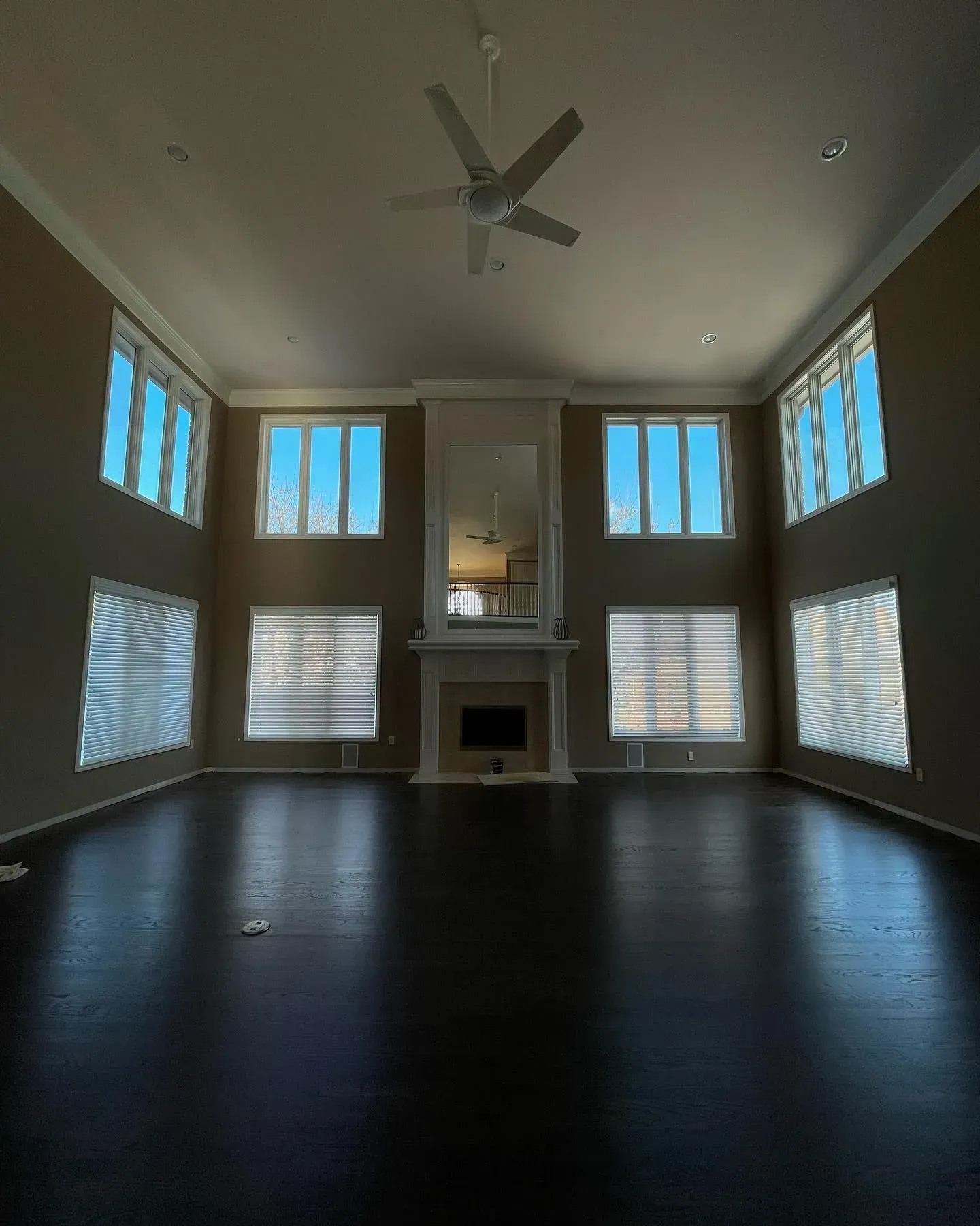 Empty living room with dark floors, tall windows, a fireplace, and a ceiling fan