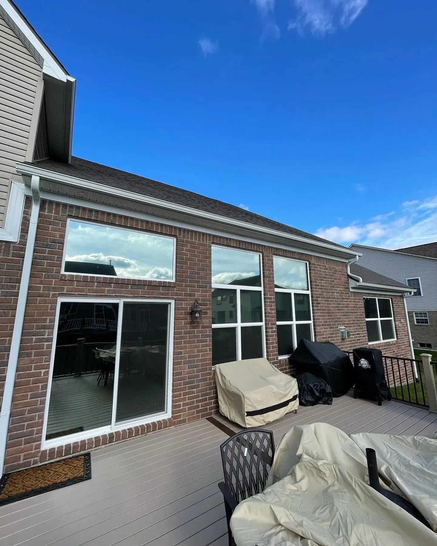Brick patio beside house with large windows, outdoor furniture, and a bright blue sky