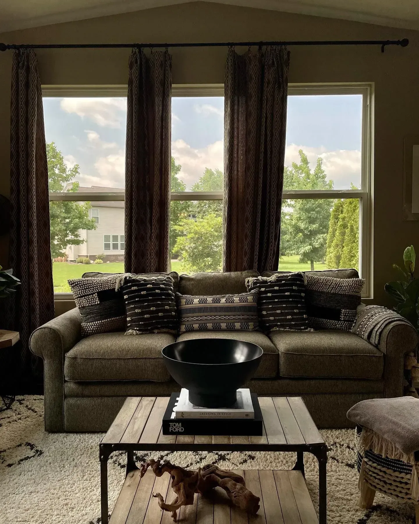 Living room with sofa, coffee table, patterned curtains, and large windows overlooking greenery