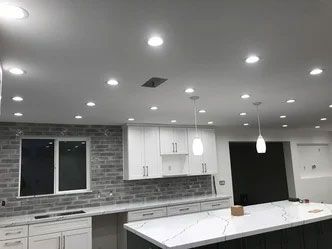 A kitchen with white cabinets , a large island , and a brick wall.