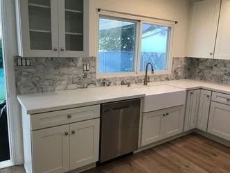 A kitchen with white cabinets , a stainless steel dishwasher , a sink , and a window.
