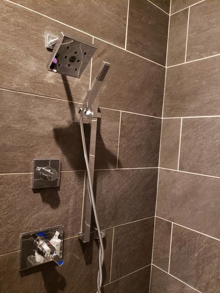 Shower with dark brown tiled walls and silver fixtures. A square showerhead and handheld wand.