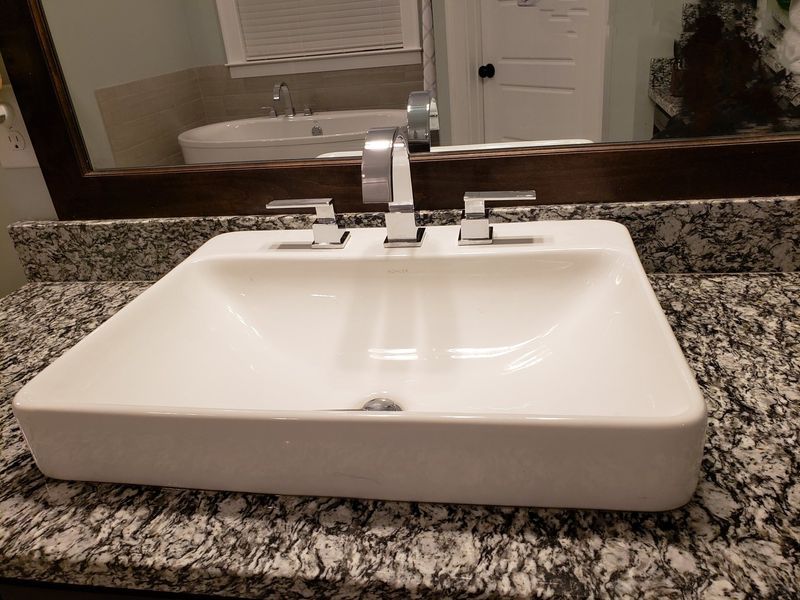 White bathroom sink with chrome faucet on a granite countertop; mirror reflects a bathtub.