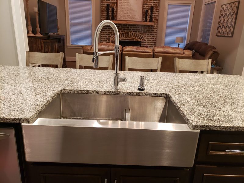 Stainless steel farmhouse sink in kitchen with granite countertop and faucet.