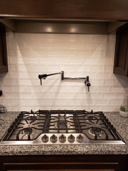 Gas stovetop in kitchen, with black pot filler against white brick backsplash.