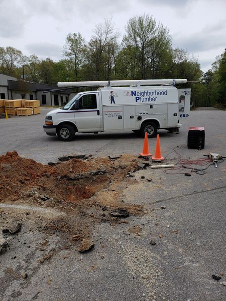 White plumbing truck parked next to a broken section of asphalt. Two orange cones are placed near the damaged road.
