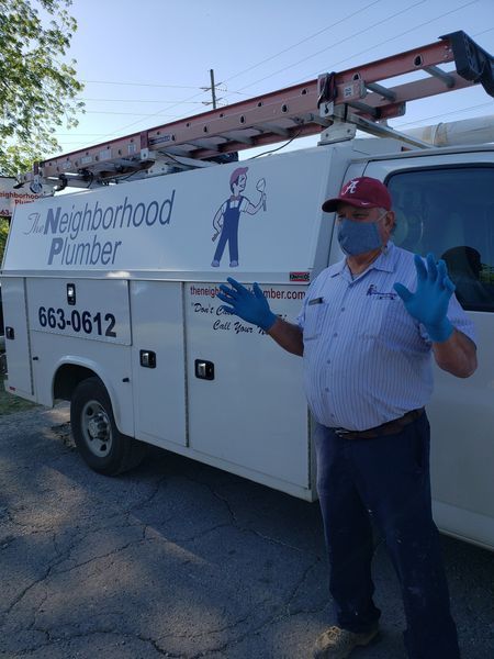 Plumber by truck, wearing mask and gloves. The truck has the company name 