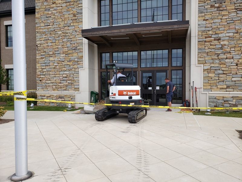 Construction at a building entrance. A small Bobcat excavator is being operated near the door.