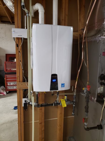 A white, wall-mounted tankless water heater with display, installed on a wooden frame.