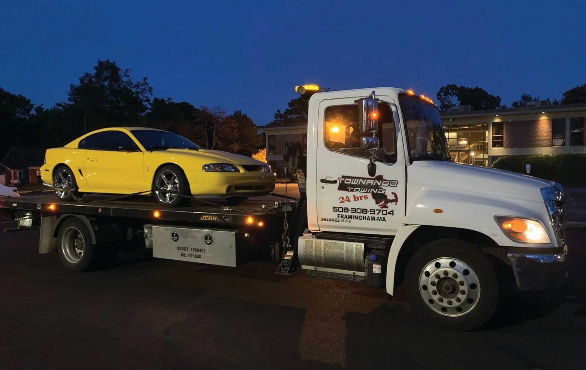 Yellow Mustang on flatbed tow truck at night.