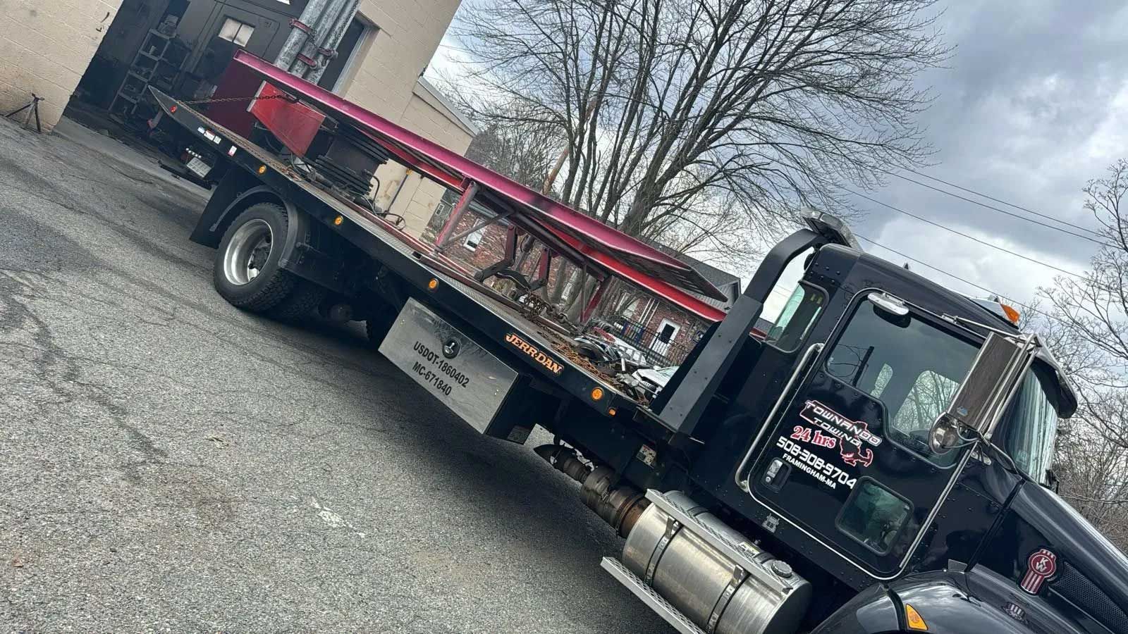 Black tow truck with a flatbed parked on asphalt, with red storage units visible.