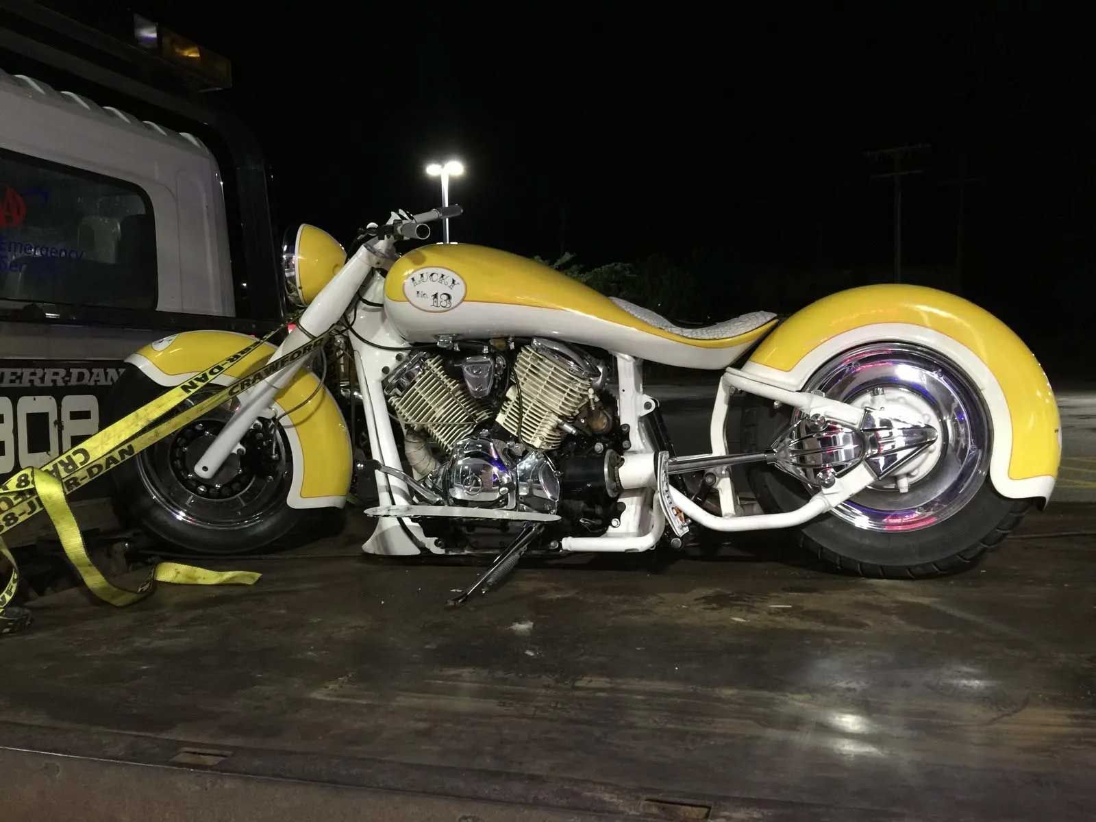 Yellow and white custom motorcycle strapped to a tow truck bed at night.