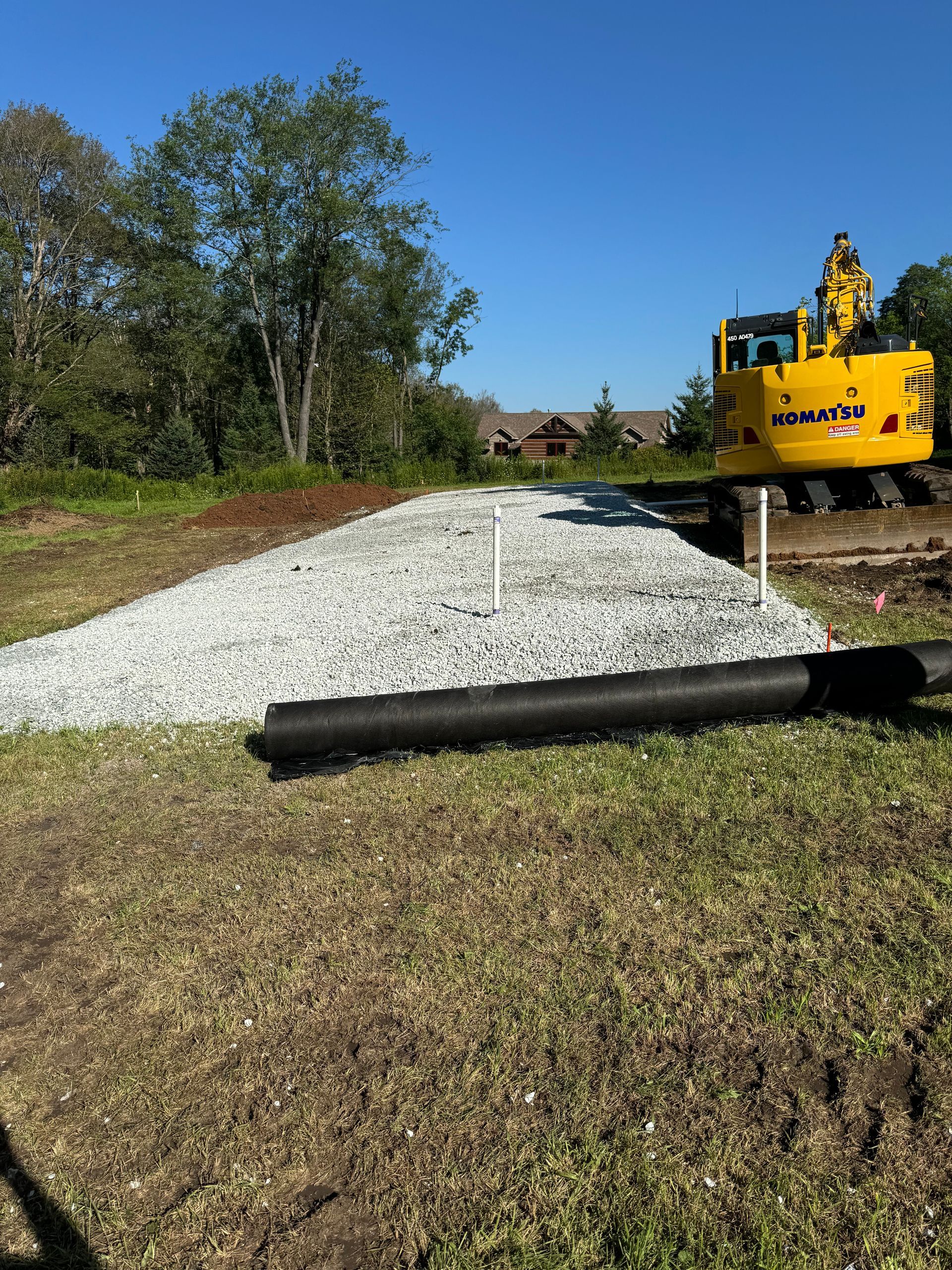 A yellow excavator is working on a gravel road.
