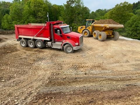 A red dump truck is driving down a dirt road next to a yellow dump truck.
