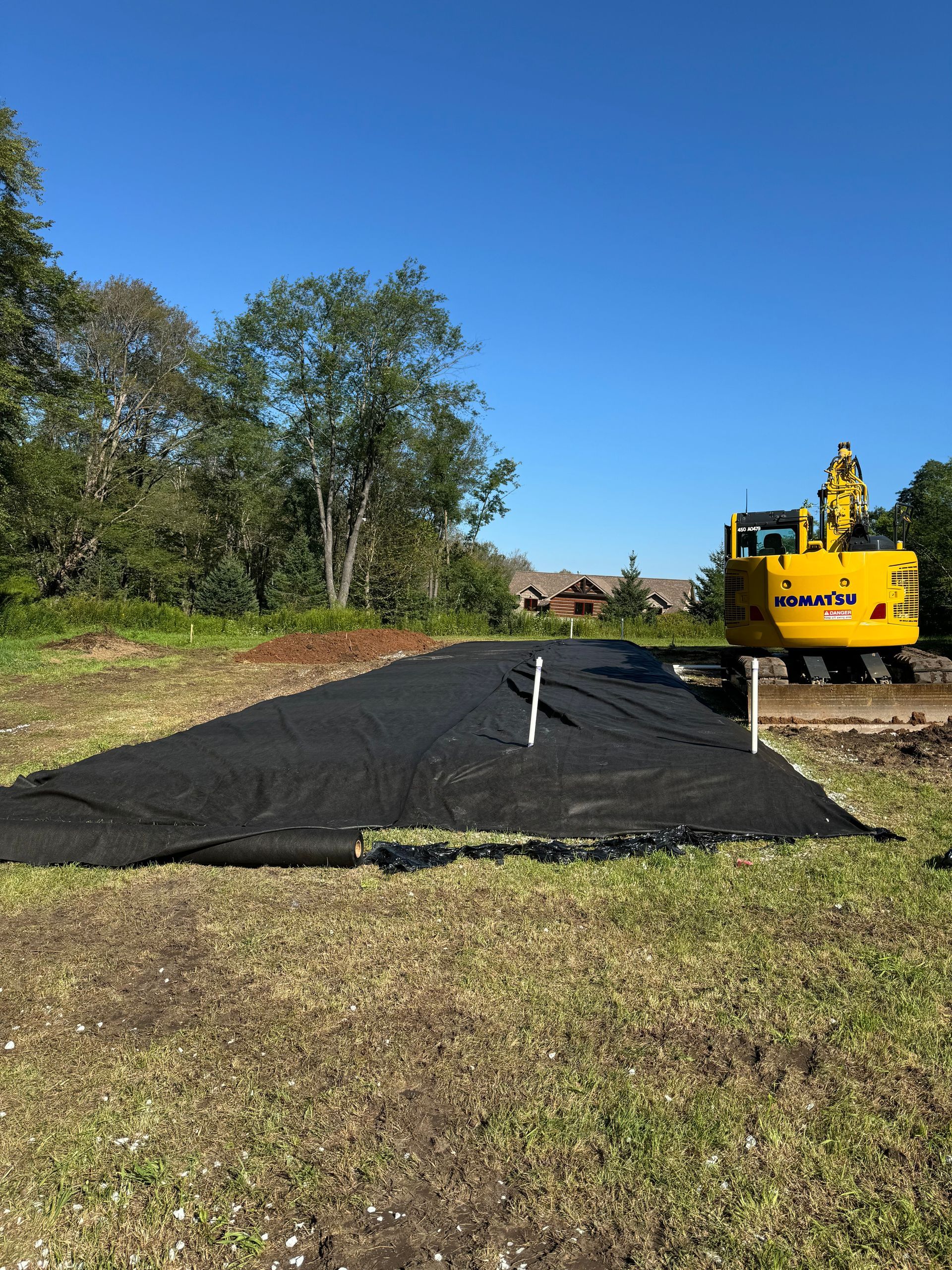 A yellow excavator is sitting in the middle of a grassy field.