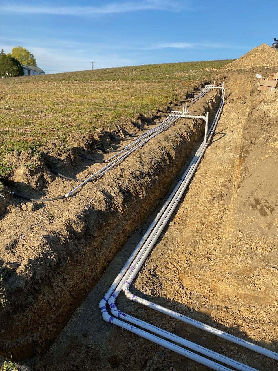 A bunch of pipes are laying in the dirt in a trench.