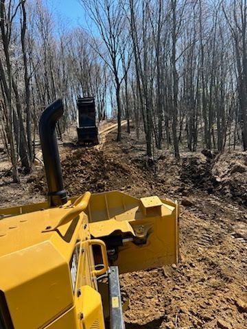 A bulldozer is moving dirt on a dirt road in the woods.