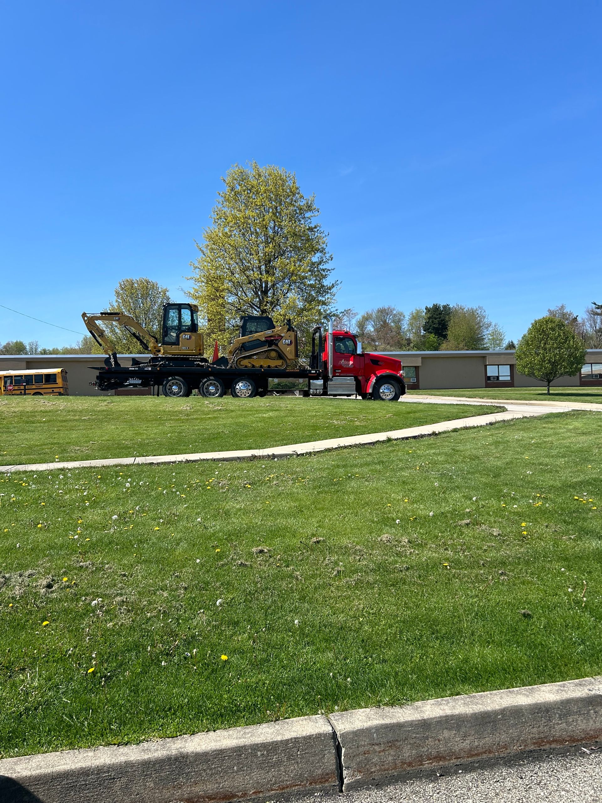 A red truck is towing a bulldozer in a grassy field.