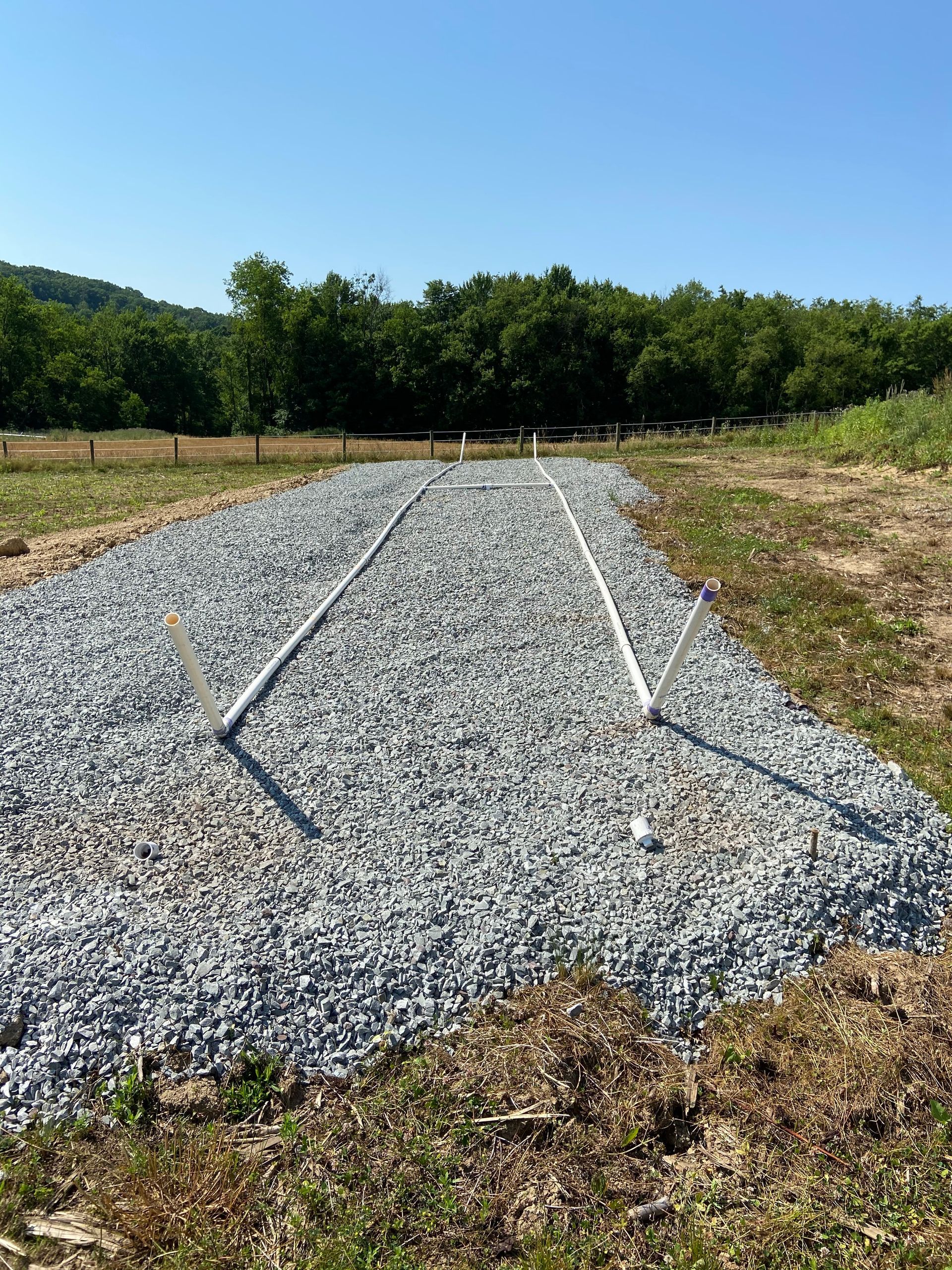 A gravel road in a field with trees in the background