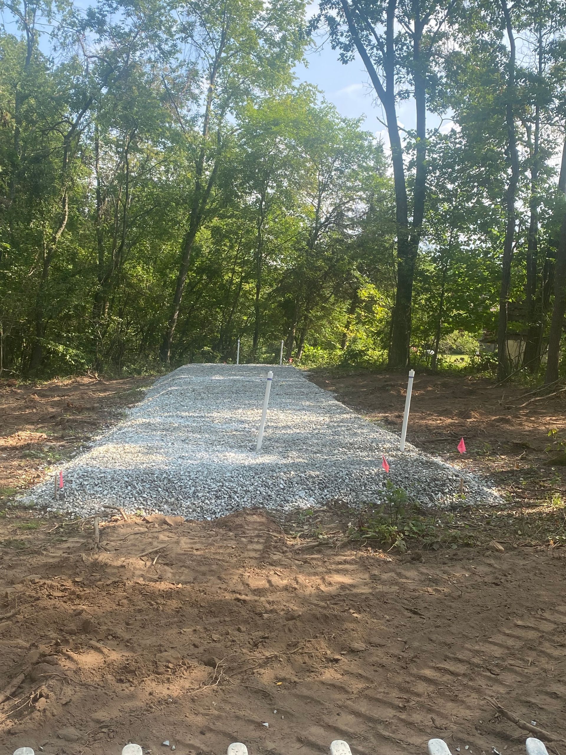 A pile of gravel is sitting in the middle of a dirt field surrounded by trees.