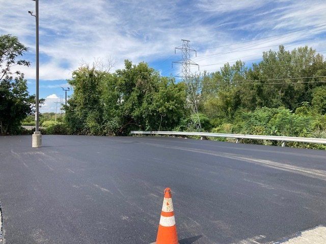 An orange and white traffic cone is sitting on the side of a road.