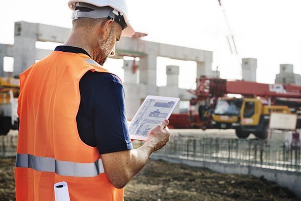A construction worker is looking at a tablet at a construction site.