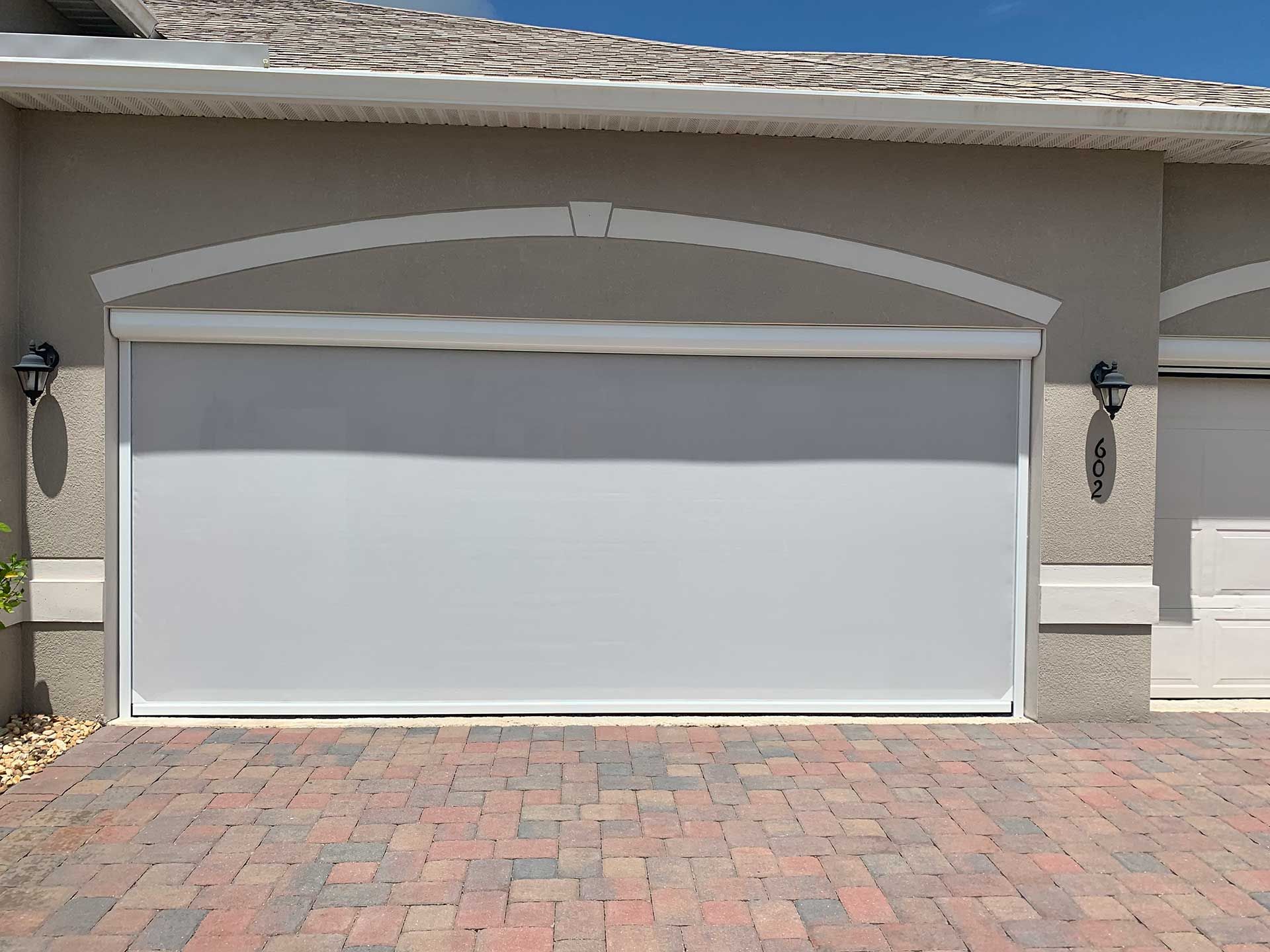 White garage screen on a stucco house with a brick driveway and two wall lanterns