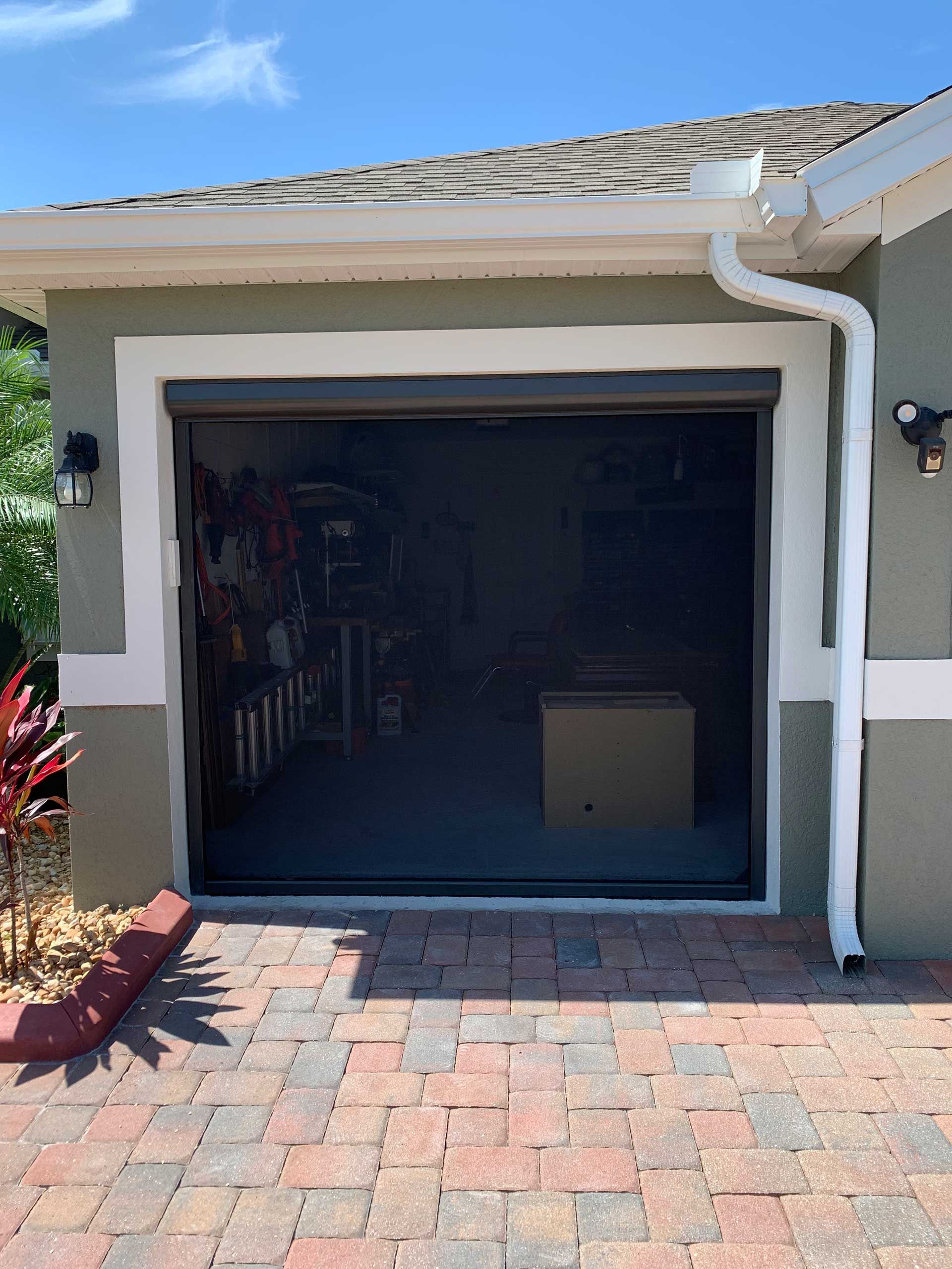Open garage door on a house with a brick driveway and white trim under a blue sky