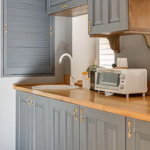 A kitchen with gray cabinets , a sink , a toaster oven , and a window.